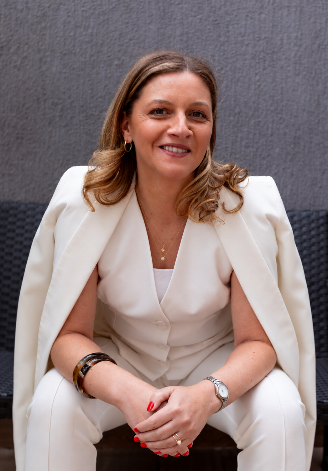 Luana Pinheiro Amaral sentada, sorrindo, com as mãos cruzadas sobre o colo, vestindo um look branco.
